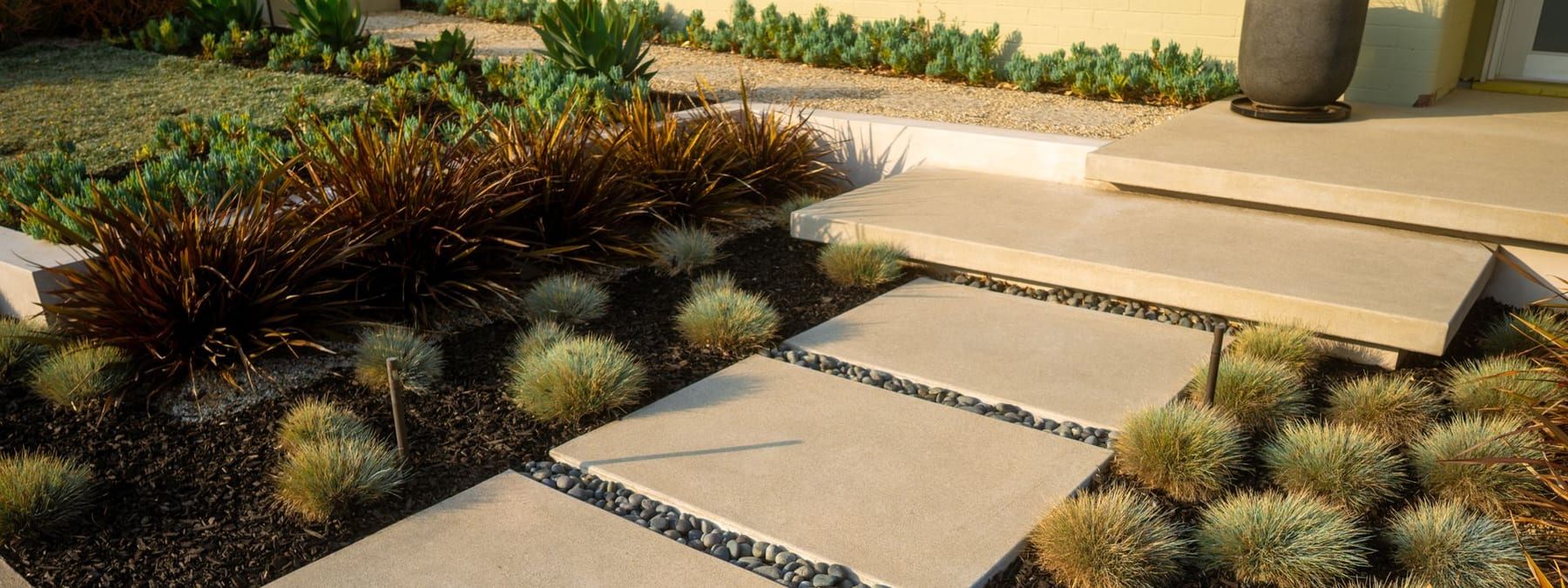 Concrete stepping pads through a drought-tolerant front yard with ornamental grasses and succulents
