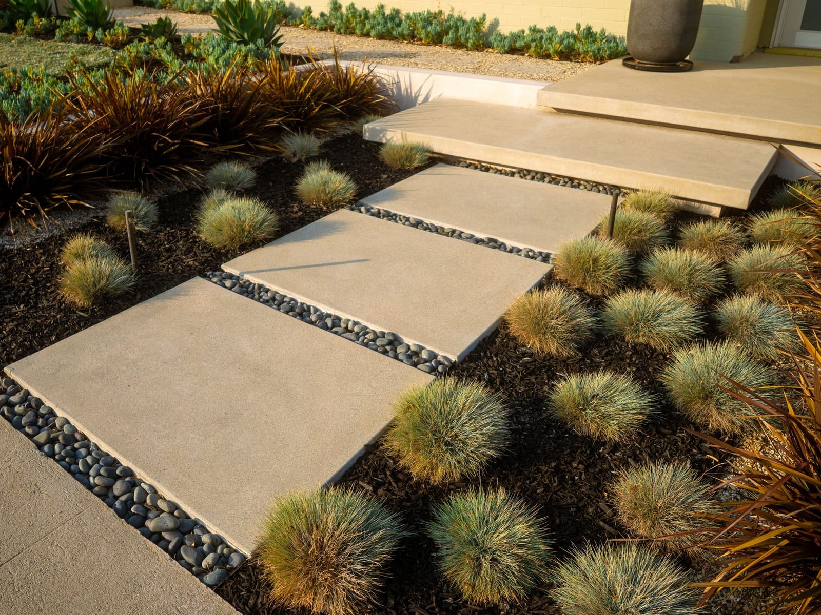 Concrete stepping pads through a drought-tolerant front yard with ornamental grasses and succulents