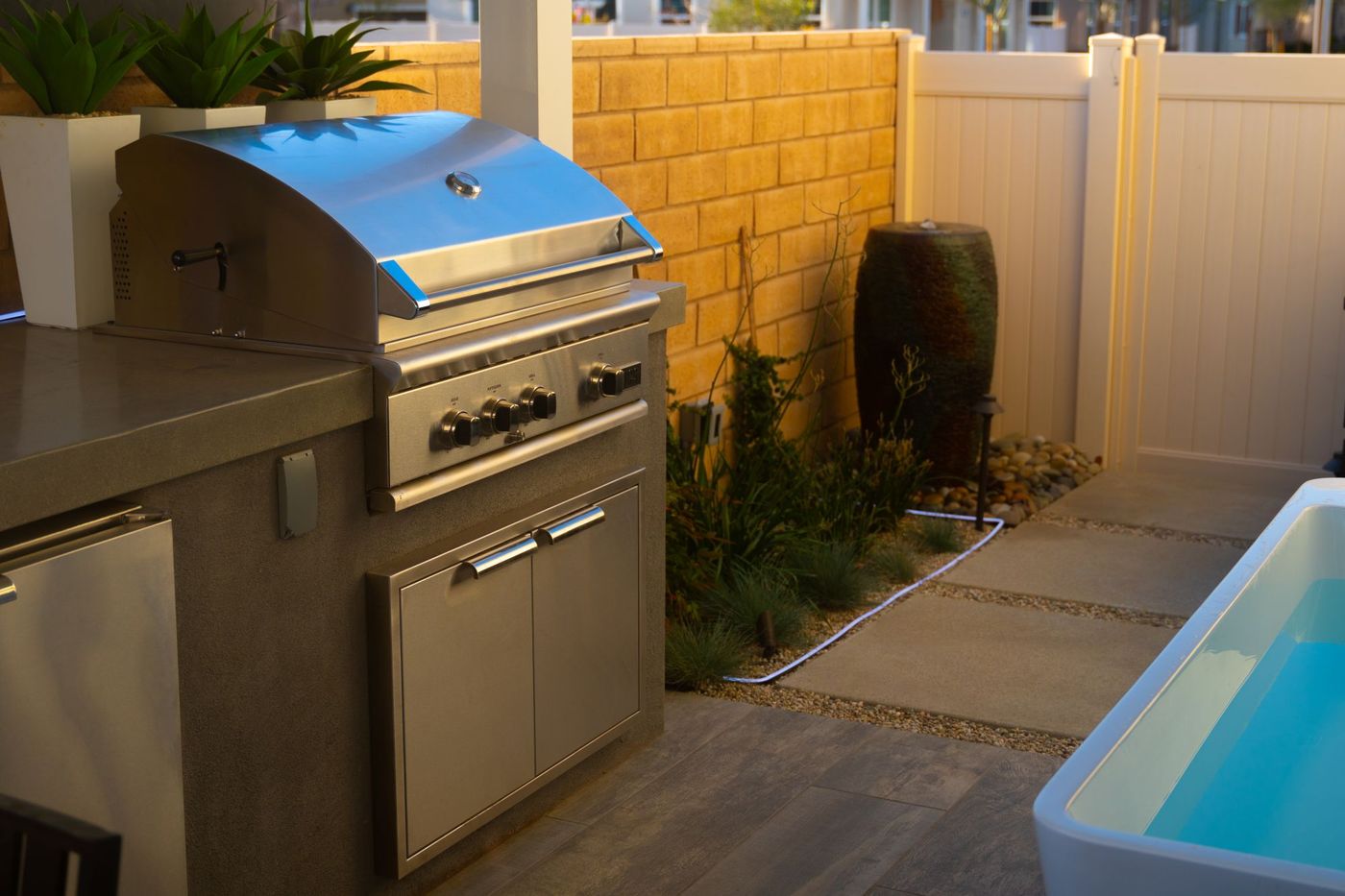 Compact outdoor living design featuring a built-in stainless steel grill, concrete countertop, and modern plunge pool beside landscaped planting.