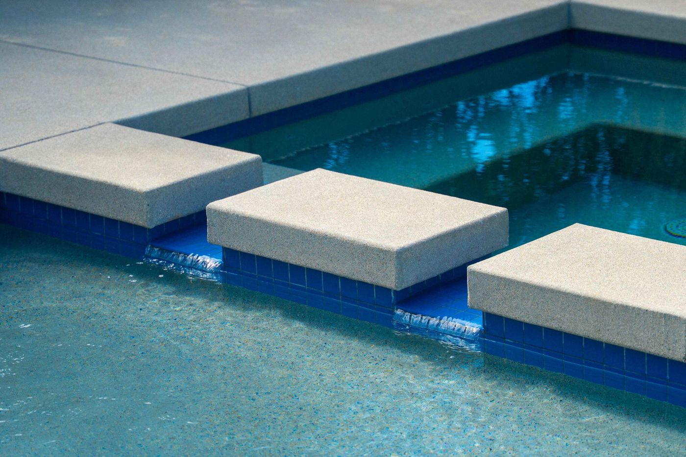 Close-up of square stepping pads leading across a spa and swimming pool with blue tile interior.