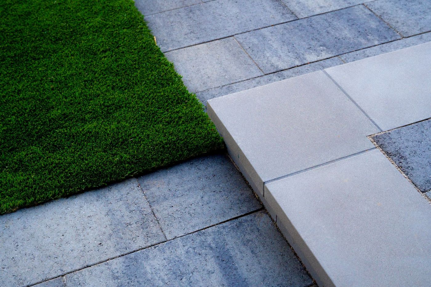 Clean transition step between artificial turf and stone paver patio in a contemporary outdoor design.