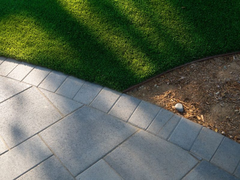 Close-up of synthetic turf meeting geometric concrete pavers and mulch planting bed, showing clean edging detail in a contemporary California landscape.