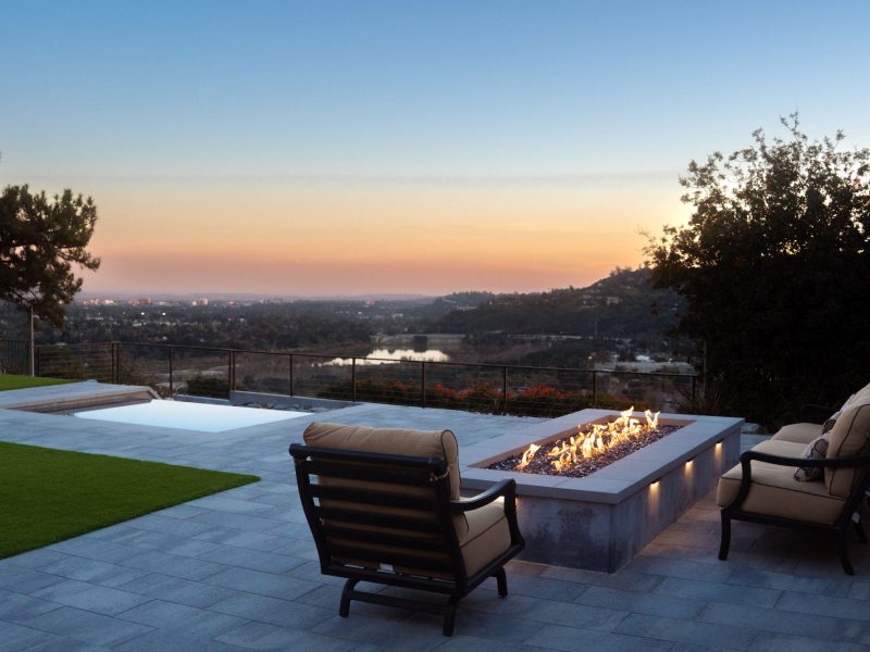 Outdoor fire pit seating area with cushioned chairs overlooking distant city lights at dusk.