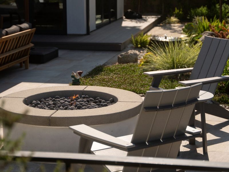 Round concrete fire pit surrounded by Adirondack chairs and drought-tolerant planting in a modern backyard design.