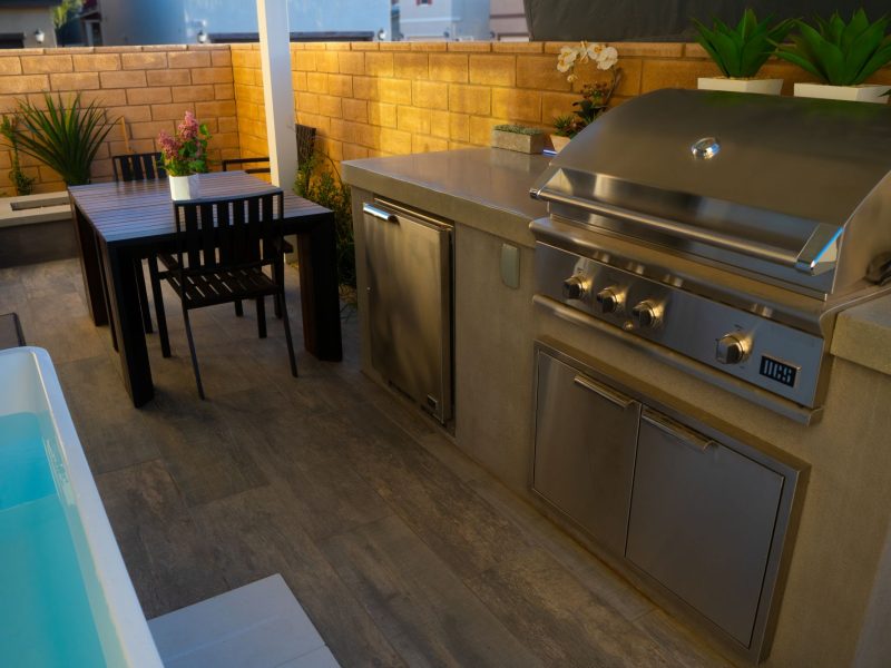 Modern small-space outdoor kitchen featuring stainless steel grill, integrated storage, and concrete counter adjacent to plunge pool.