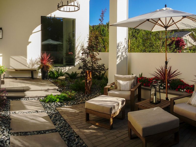 Cozy courtyard patio with cushioned chairs, umbrella shade, stepping stone path, and decorative planting.