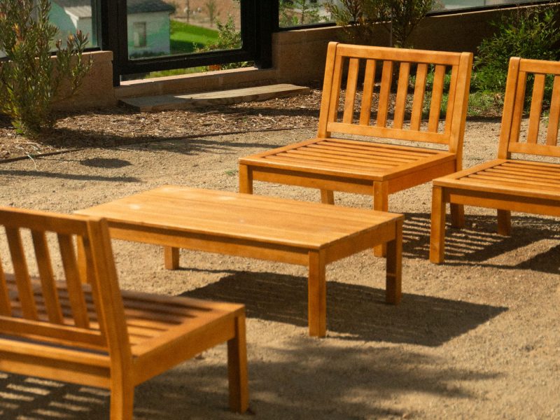 Close view of wooden outdoor seating arranged on decomposed granite within a landscaped courtyard garden overlooking surrounding homes and hills.