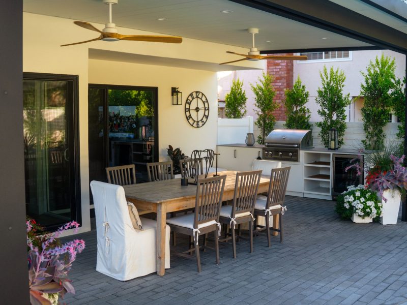 Covered backyard patio featuring dining table, ceiling fans, and built-in outdoor kitchen for entertaining.