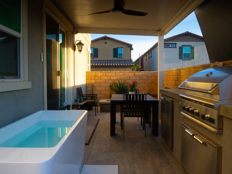 Shaded patio with dining table, ceiling fan, outdoor kitchen, and rectangular plunge pool in a narrow backyard layout.