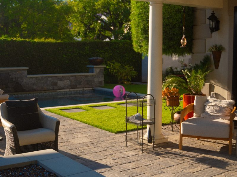Outdoor patio with seating area, plants, and view of a landscaped backyard swimming pool.