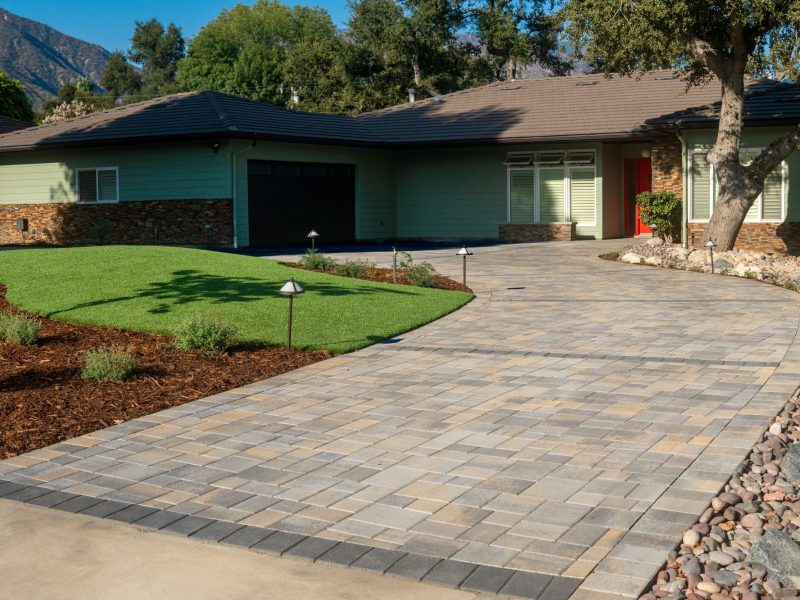 Residential front yard featuring curved paver driveway, green turf lawn, landscape lighting, and modern home facade in a California design-build project.
