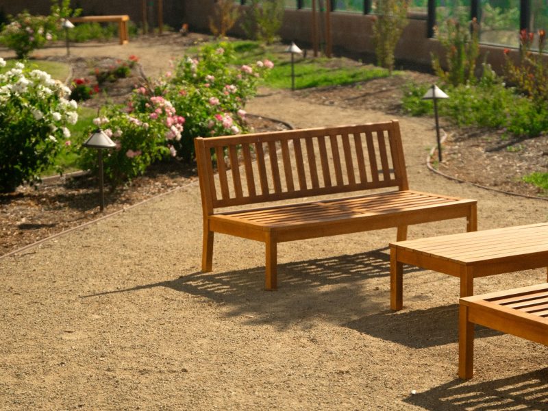 Wood bench seating beside blooming flower beds and winding decomposed granite walkway in a serene residential courtyard landscape.