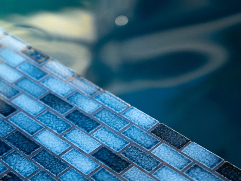 Detailed view of blue glass tile pool coping and water surface in a contemporary backyard swimming pool.