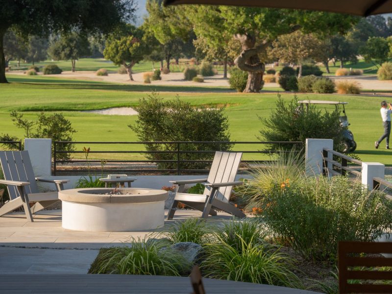 Modern backyard patio featuring circular fire pit seating and open views overlooking a green golf course landscape.