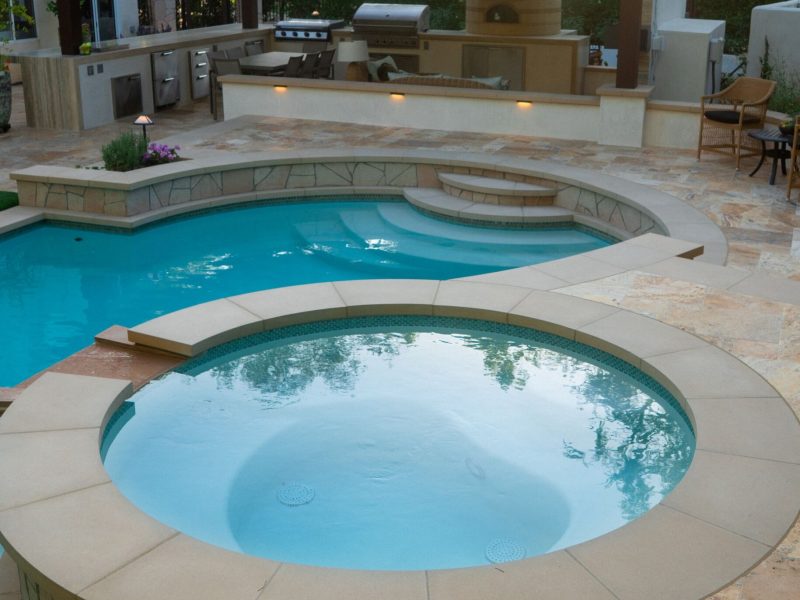 Close view of round spa connected to freeform swimming pool with natural stone coping and patio in a luxury residential backyard.