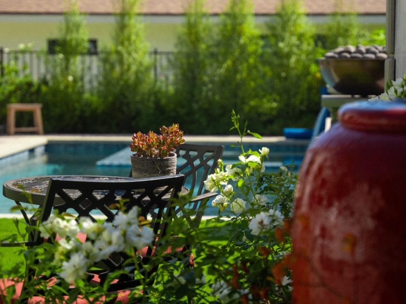 Outdoor patio seating area with decorative plants overlooking a modern residential swimming pool and landscaped garden.