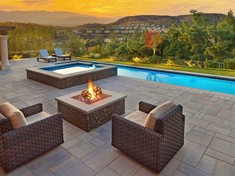 Modern swimming pool with spa, fire pit seating area, and panoramic sunset hillside view in a luxury backyard.