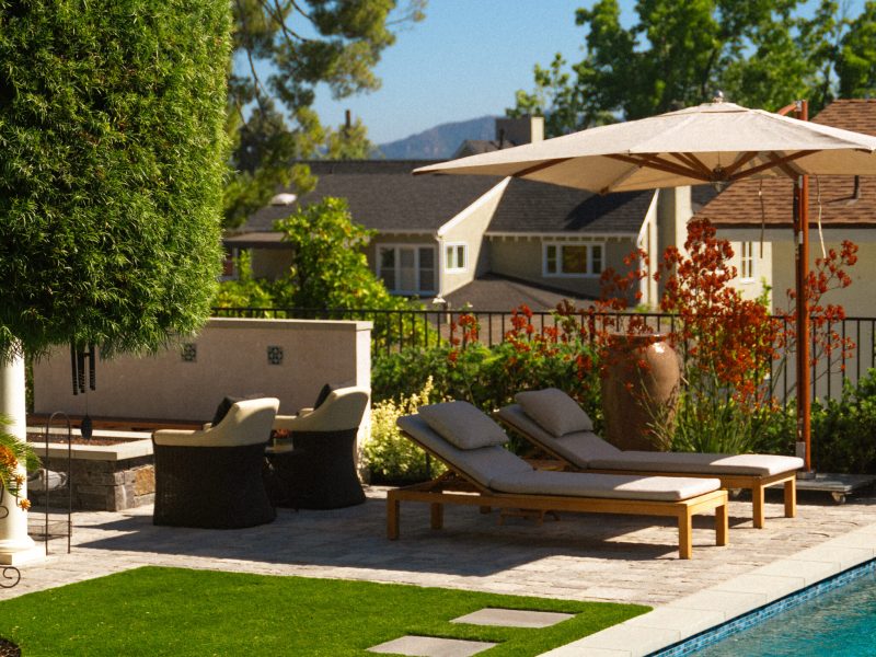 Poolside lounge chairs and patio umbrella beside a modern swimming pool in a professionally landscaped backyard.