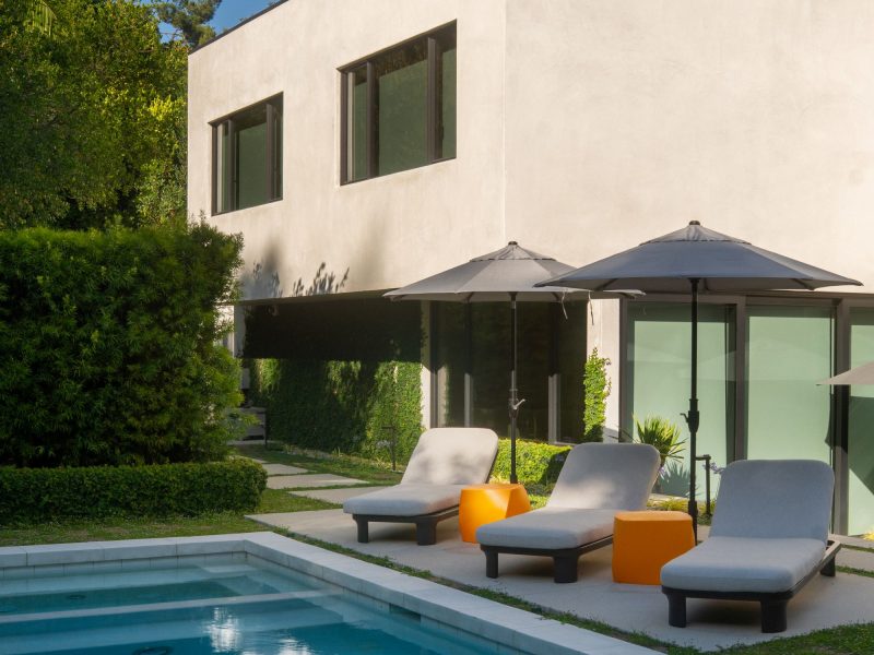 Contemporary backyard featuring a rectangular swimming pool, cushioned lounge chairs, umbrellas, and modern stucco home architecture.