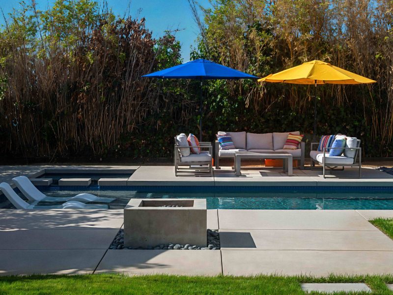 Contemporary swimming pool with tanning ledge, fire feature, and outdoor seating area in a landscaped backyard.