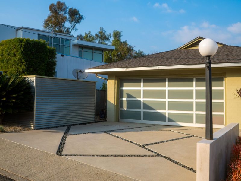 Close view of a modern concrete driveway with geometric joint pattern, and minimalist hardscape landscaping in a California residential front yard.