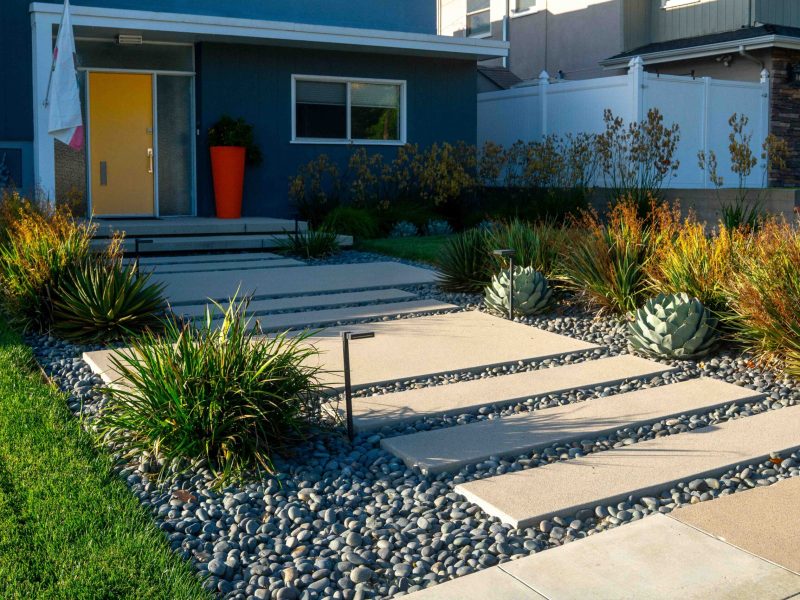 Residential front yard landscape featuring floating concrete steps, river rock ground cover, and drought-tolerant plants.
