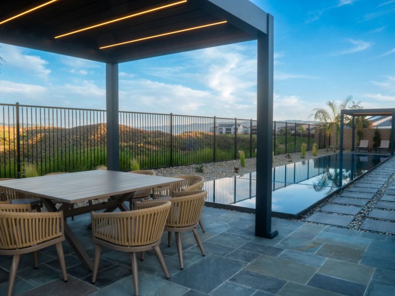 Minimalist pergola structure with lounge seating beside pool and decorative grasses framed by panoramic hillside scenery.