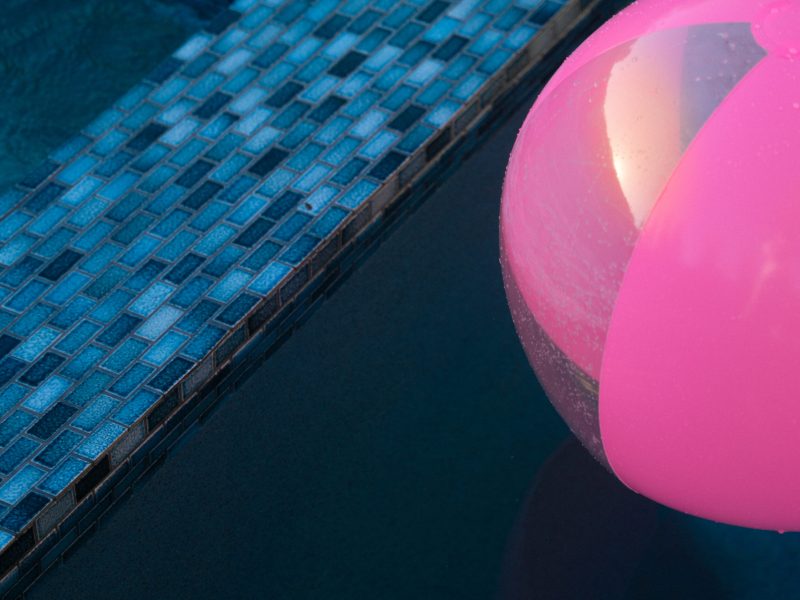 Close-up of blue glass pool tile edge with a pink inflatable pool float in clear swimming pool water.