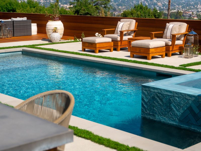 Clear blue swimming pool water beside contemporary patio seating, decorative planters, and clean-lined landscape design.