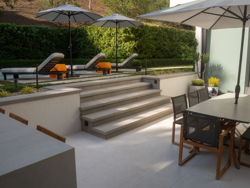 Concrete steps leading from patio dining space to pool lounge area surrounded by manicured landscape.