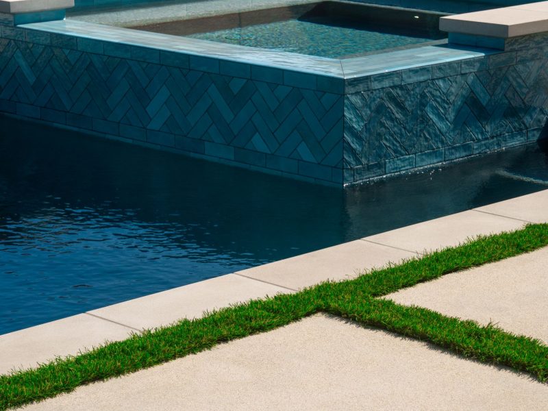 Contemporary raised spa with blue herringbone tile facing, clean concrete coping, and adjacent swimming pool waterline detail.