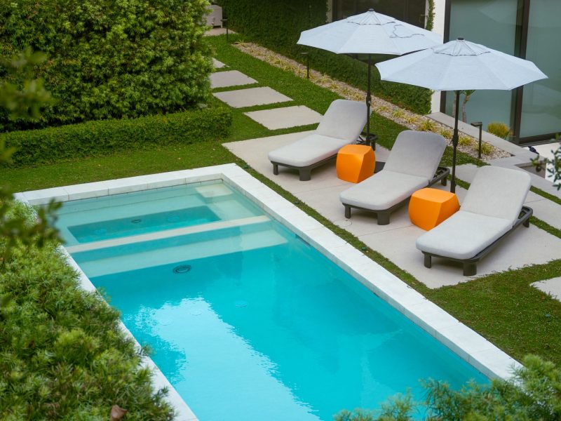 Overhead perspective of turquoise rectangular pool with cushioned lounge chairs and geometric stepping stones.