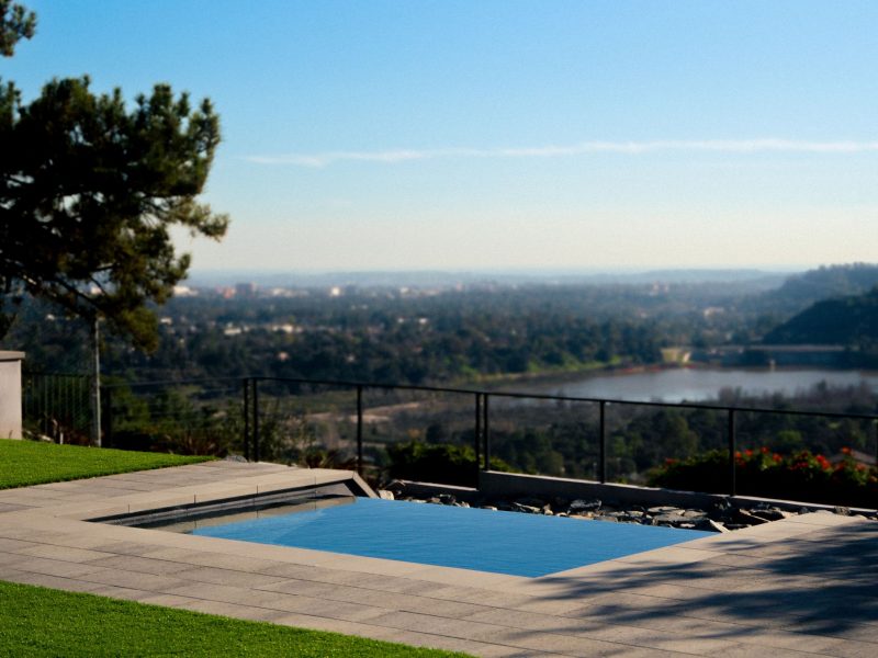 Square backyard spa overlooking lake, trees, and distant skyline in a contemporary landscape design.