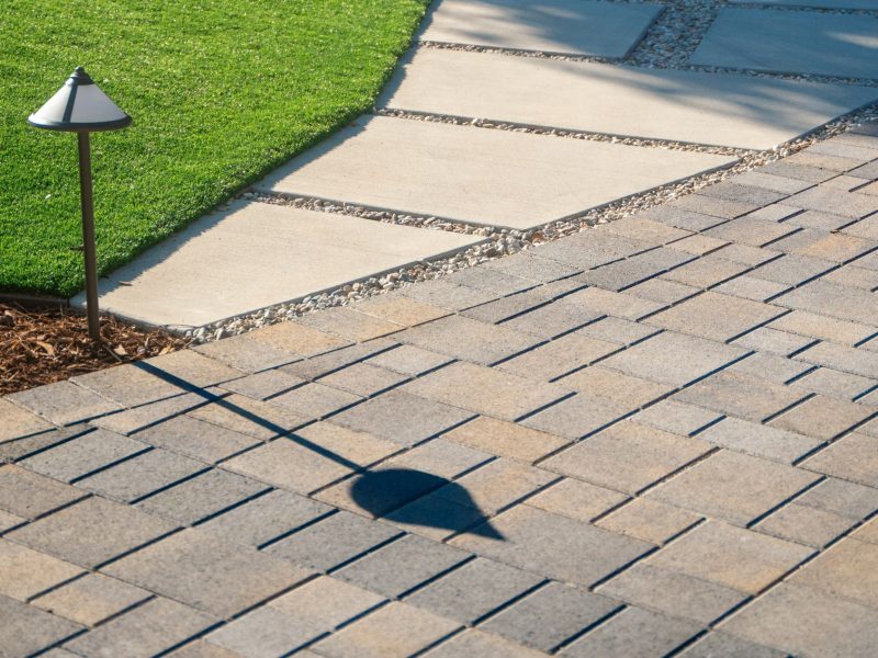 Concrete stepping stone path bordered by gravel joints and adjacent paver driveway, highlighting clean geometric hardscape design in a contemporary landscape.