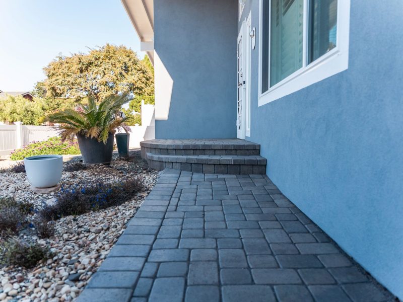 Custom paver driveway installation in Morro Bay featuring a small retaining wall and white privacy fence.