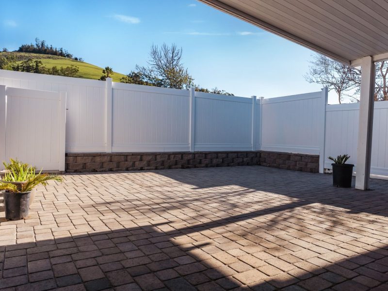 Interlocking paver driveway extending along the side yard of a Morro Bay home with white vinyl fencing.
