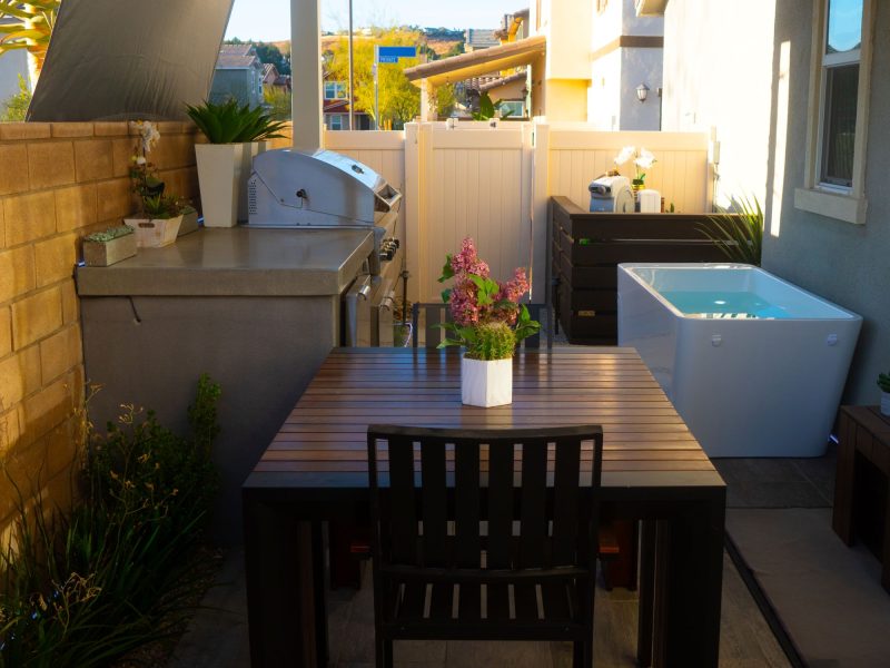 Efficient small-yard design combining outdoor dining table, built-in grill kitchen, privacy fencing, and modern plunge pool.