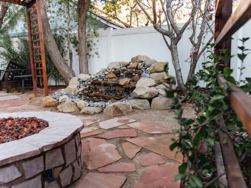 Close-up of tiered natural stone waterfall surrounded by river rock in a backyard patio setting.