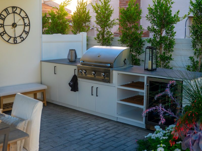 Custom outdoor kitchen with built-in stainless steel grill, white cabinetry, and paved patio in a modern backyard design.