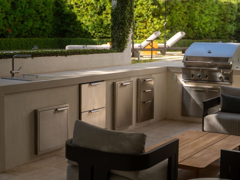 Custom outdoor kitchen featuring stainless steel grill, storage drawers, and countertop seating in a contemporary backyard.