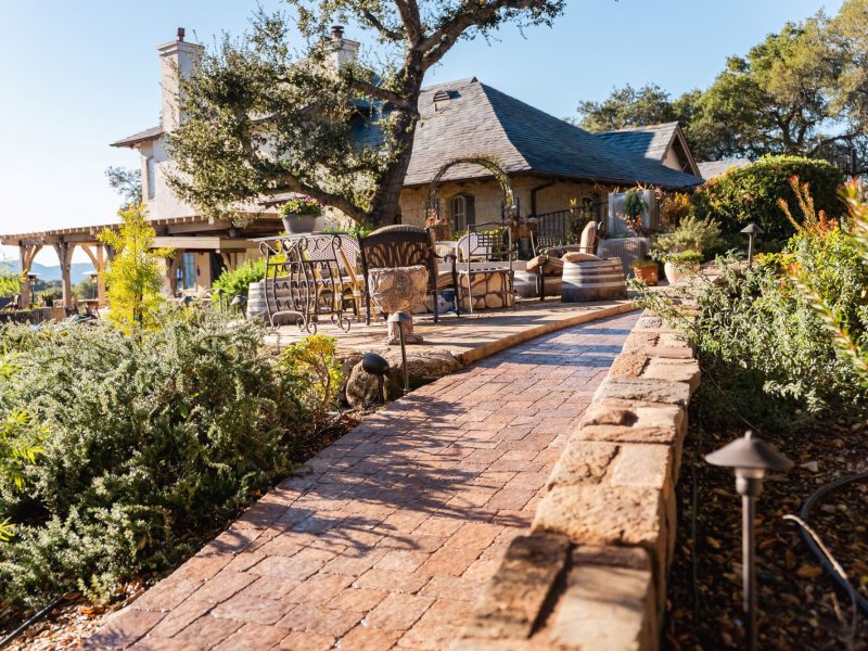 Custom paver walkway in Paso Robles leading to an elevated patio and outdoor seating area surrounded by mature oak trees.