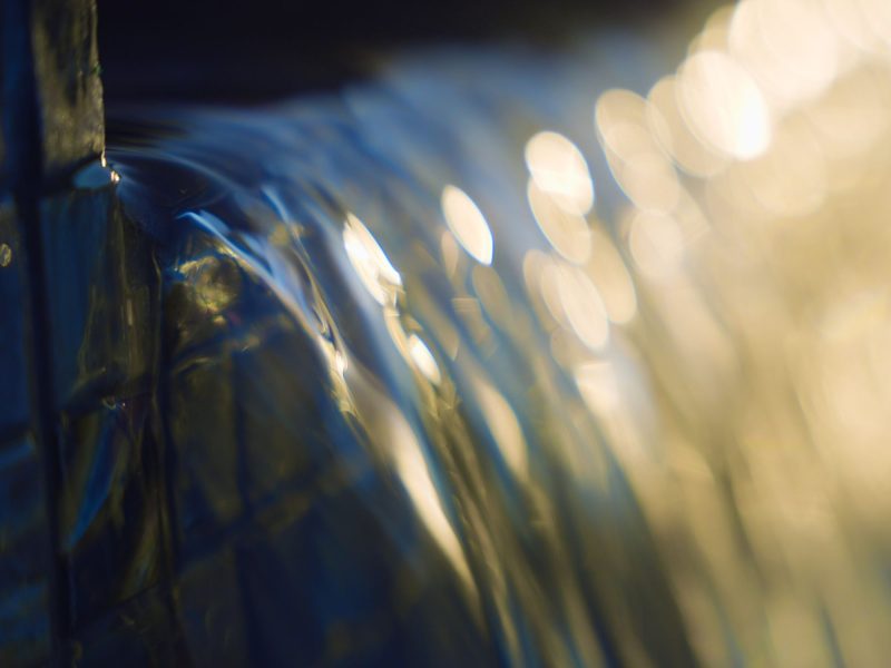Close-up of smooth water flowing over a pool spillway with soft golden light reflections.