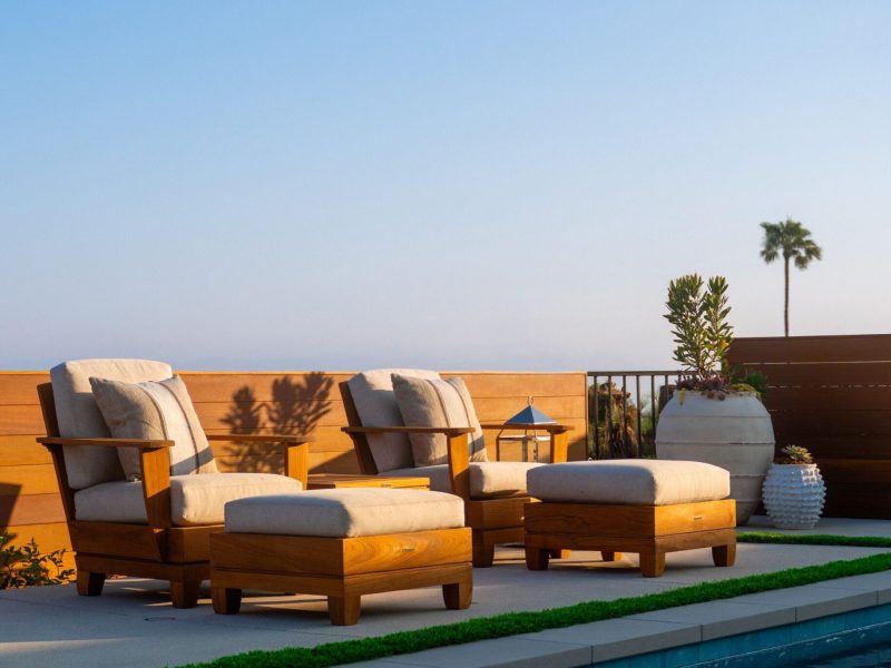 Wood-framed cushioned lounge chairs beside a contemporary swimming pool overlooking a warm sunset sky and landscaped terrace.