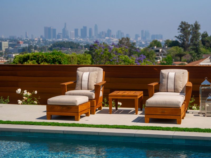Outdoor lounge chairs and side table positioned beside a modern pool with distant Los Angeles skyline and hillside landscape in the background.