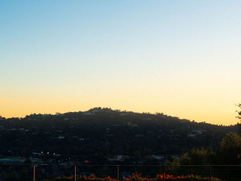 Square spa reflecting sunset sky with hillside neighborhood view beyond a modern backyard patio.