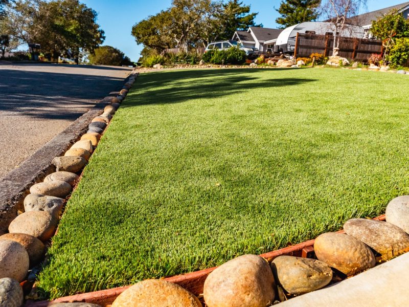 Artificial turf installation in a San Luis Obispo front yard with decorative river rock edging and clean curb transition.
