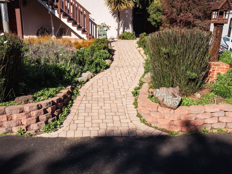 Curved paver garden pathway in San Luis Obispo bordered by decorative river rocks and landscaped shrubs.