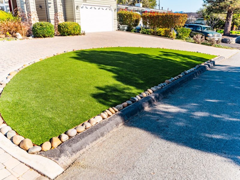 San Luis Obispo front yard featuring synthetic grass lawn bordered by river rocks and a custom paver driveway.