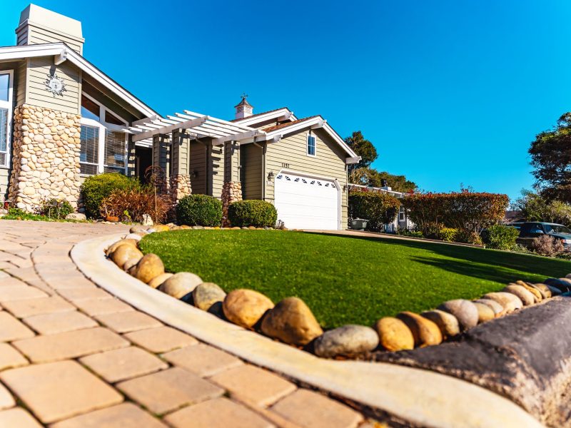 Front yard renovation in San Luis Obispo with synthetic turf lawn, decorative rock edging, and upgraded paver driveway.