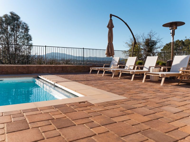Upgraded pool deck in San Luis Obispo featuring modern lounge chairs, custom paver hardscape, and panoramic hillside views.